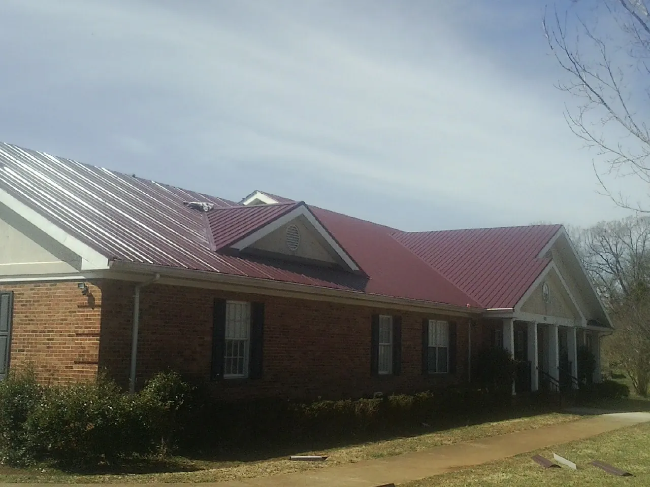 Red metal roof with gabled entries on a long brick building, from a Hail Damage Roof Repair job in Black Diamond