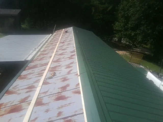 Old rusted panels beside newly installed green metal roofing — Wind Damage Roof Repair by Roofing Brothers in Black Diamond