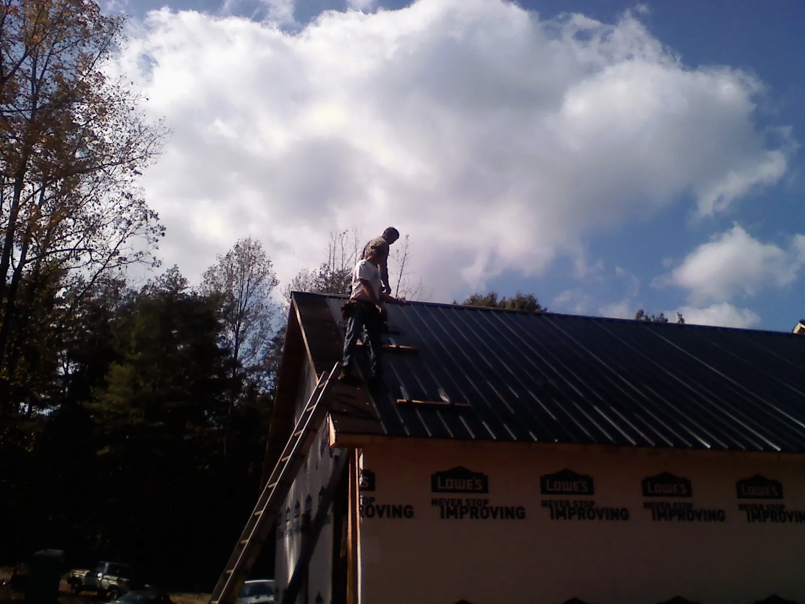 Roofer fastening dark metal panels high against a cloudy sky, from a Roof Inspection job in Black Diamond