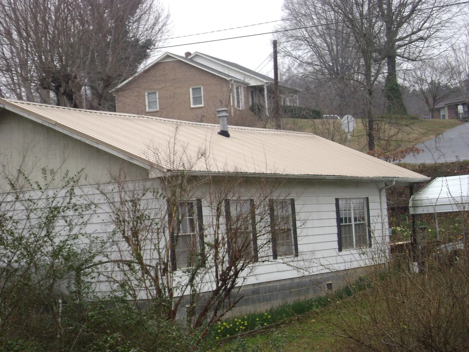 Tan metal roof on a white sided house set into a hillside — Commercial Roofing by Roofing Brothers in Black Diamond